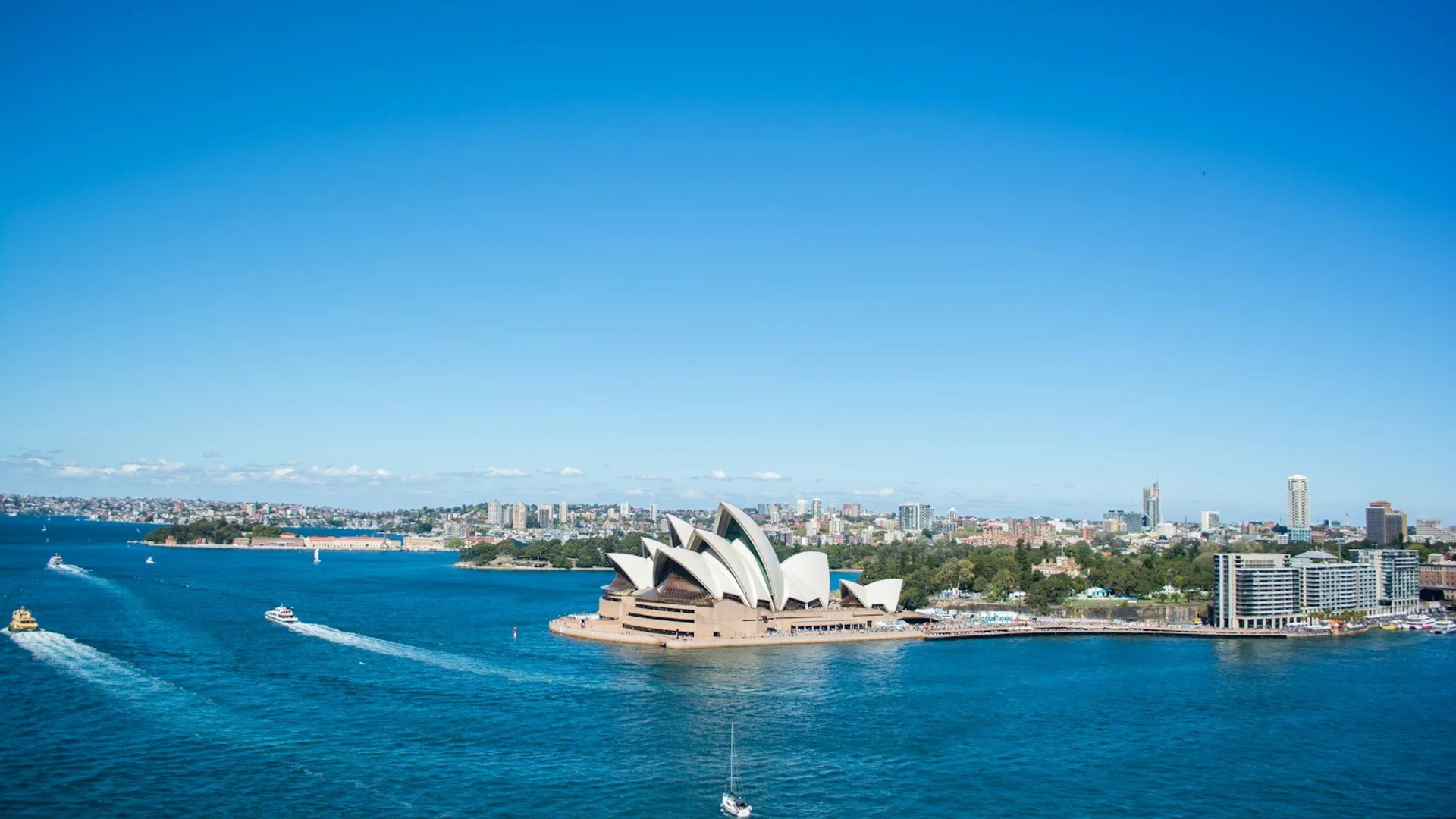 Vista aérea del Océano Pacífico con islas tropicales, la Ópera de Sídney y montañas nevadas de Nueva Zelanda