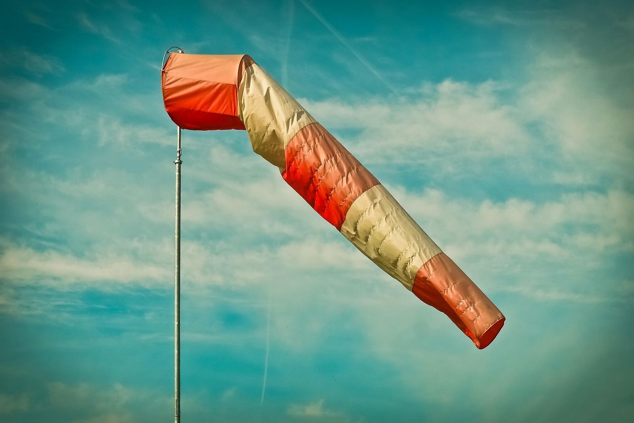 Una manga de viento roja y blanca ondeando contra un cielo azul con nubes dispersas.