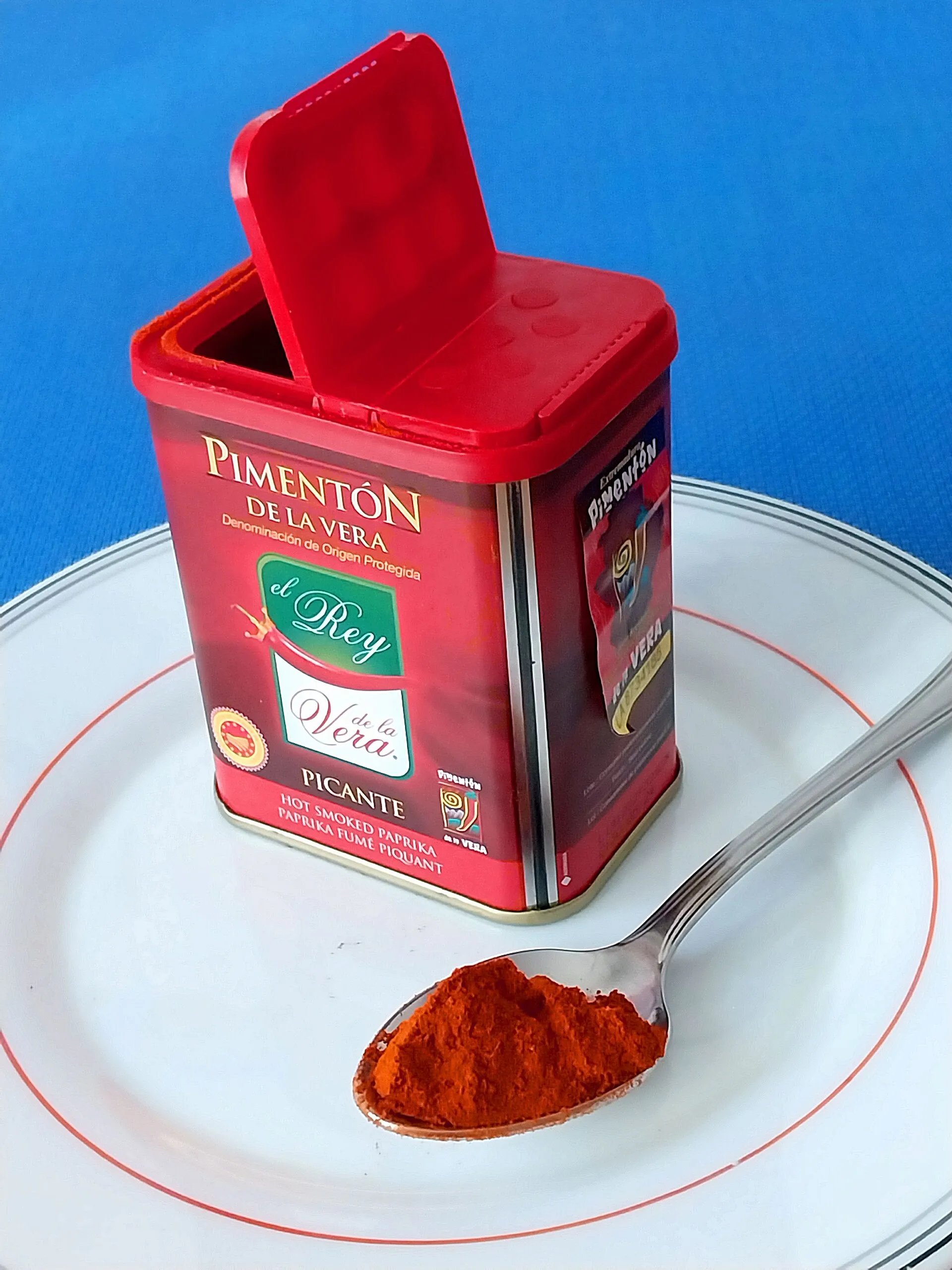 Bote rojo de pimentón de la Vera abierto con una cuchara llena de pimentón picante.