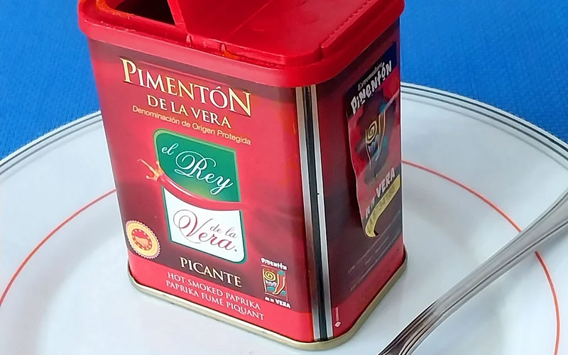 Bote rojo de pimentón de la Vera abierto con una cuchara llena de pimentón picante.