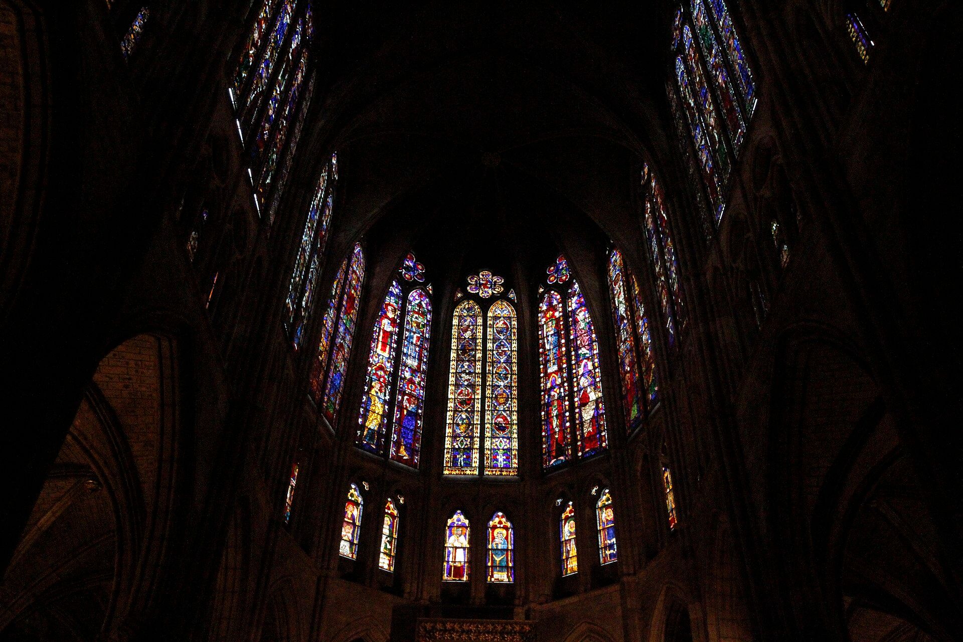 Ventanas de vidrieras coloridas y detalladas iluminadas en el interior oscuro de una catedral gótica.