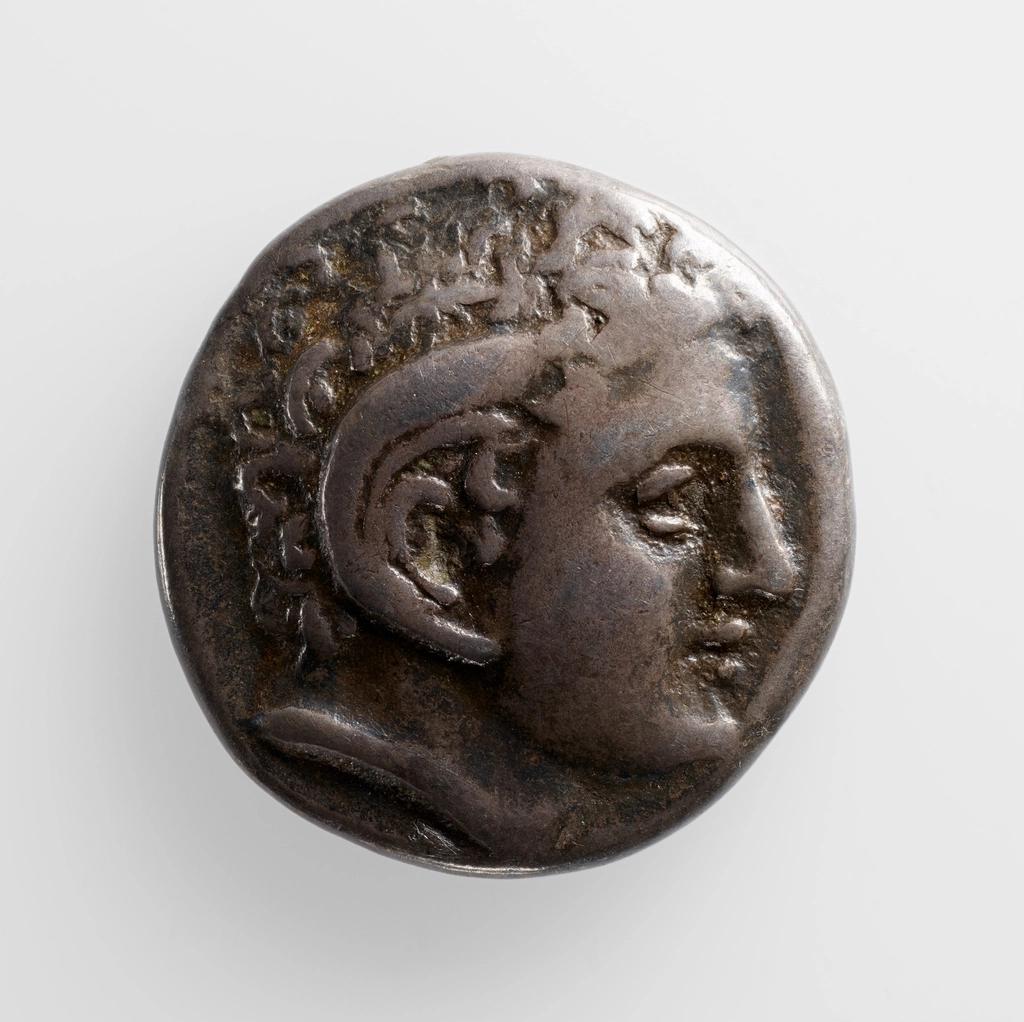 Moneda antigua de plata con el perfil de una figura humana con cabello rizado.
