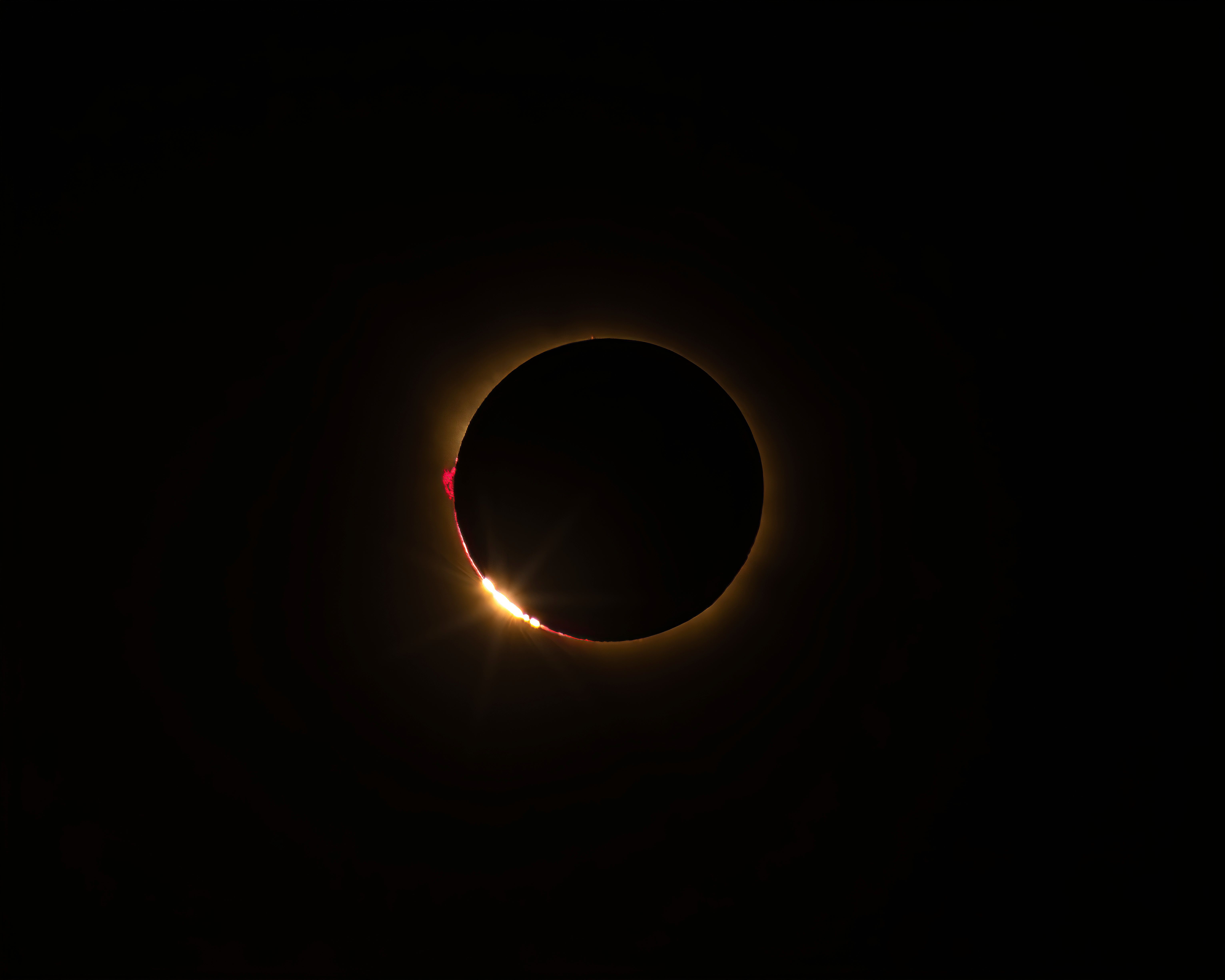 Eclipse solar total mostrando el anillo de diamante y protuberancias rojas.