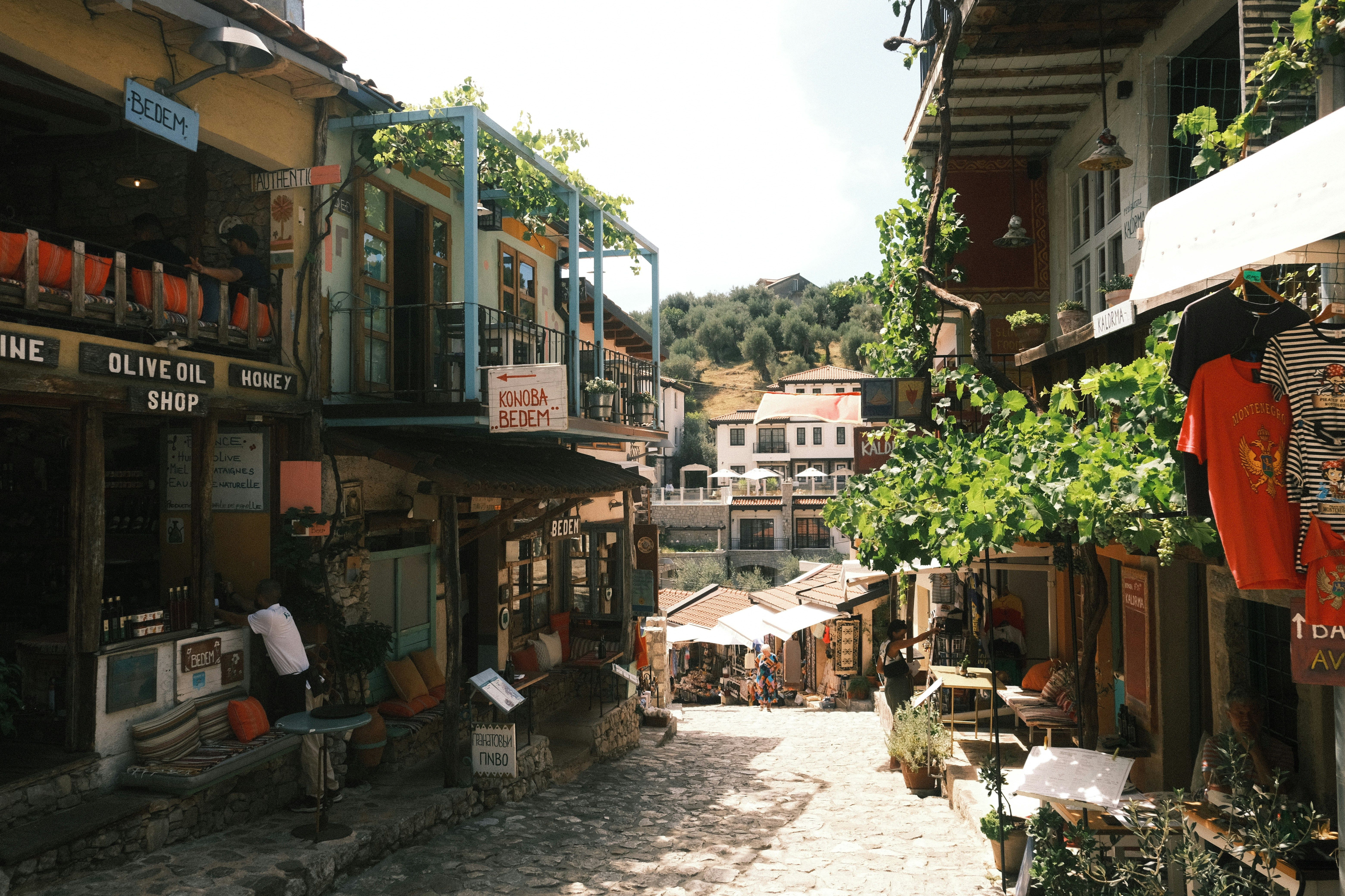 Calle empedrada en un pueblo balcánico con tiendas, restaurantes y vegetación en las fachadas.