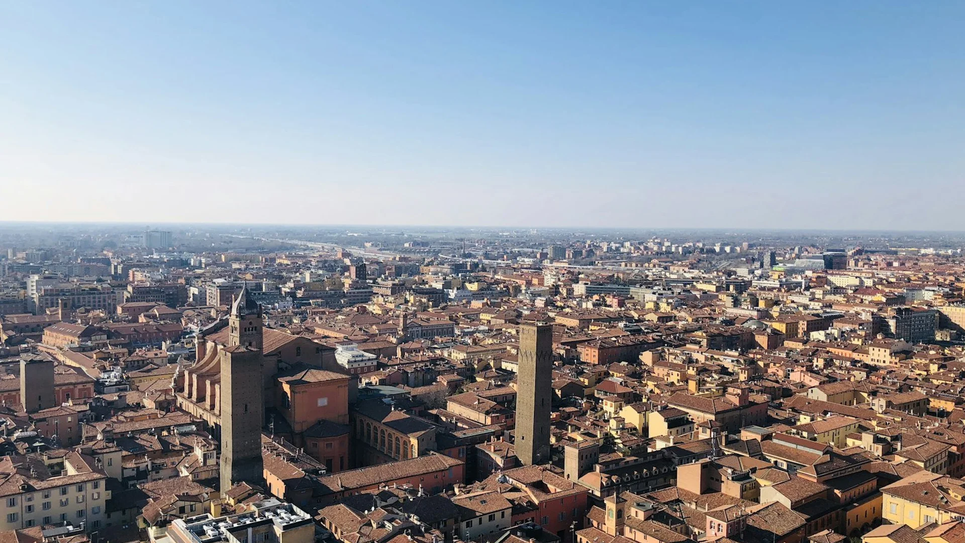 Vista panorámica de Bologna con sus características torres medievales y tejados rojos bajo la luz del atardecer
