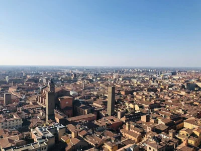 Vista panorámica de Bolonia con torres medievales y tejados rojos bajo un cielo azul claro