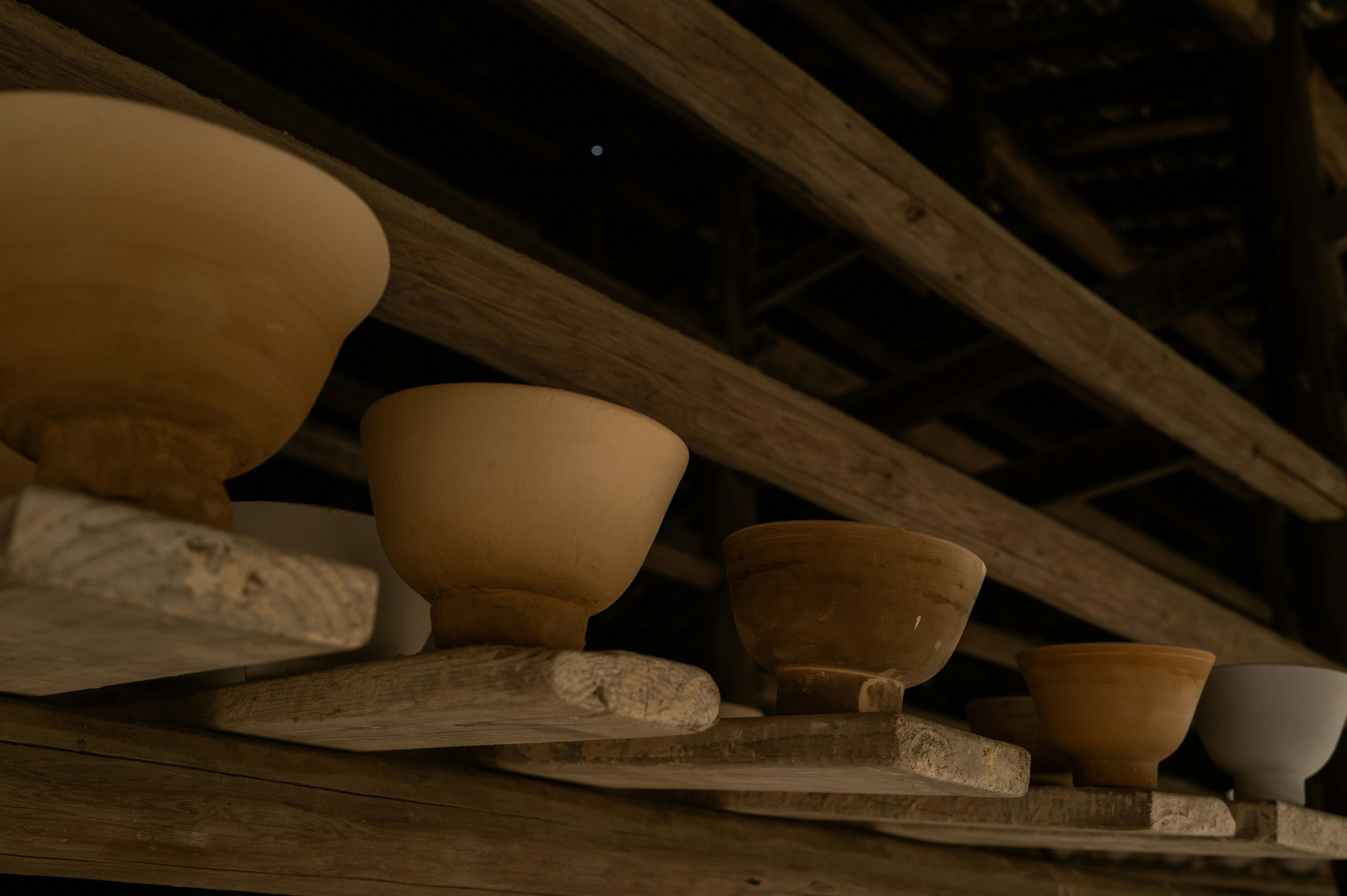 Cuencos de cerámica de diferentes tonos y tamaños sobre estantes de madera rústica.