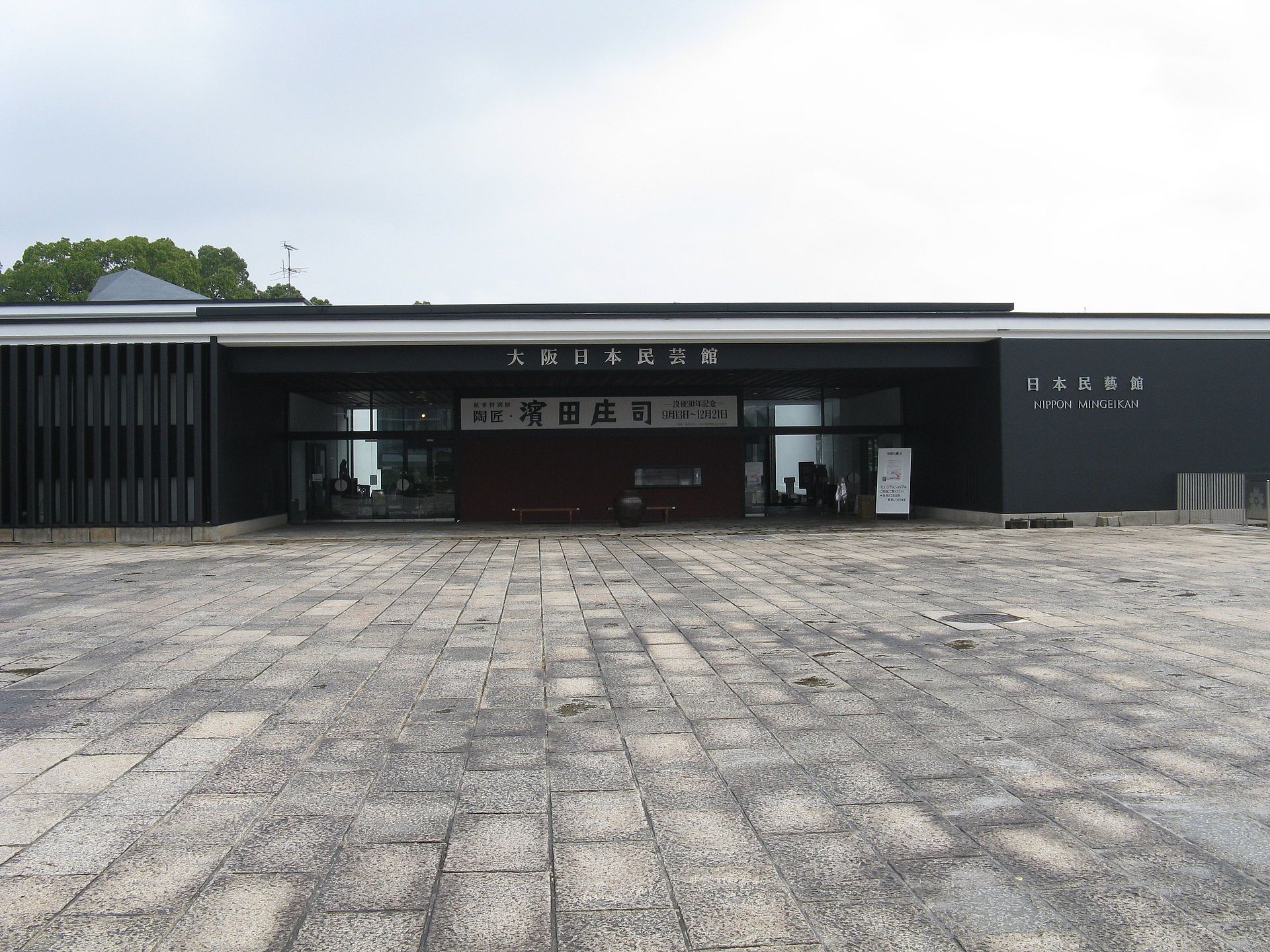 Exterior del Museo de Artesanía Popular de Japón en Osaka, con fachada oscura y patio de adoquines.