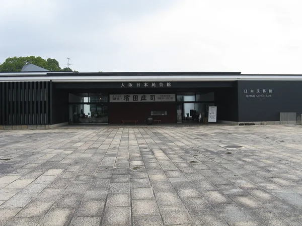 Exterior del Museo de Artesanía Popular de Japón en Osaka, con fachada oscura y patio de adoquines.