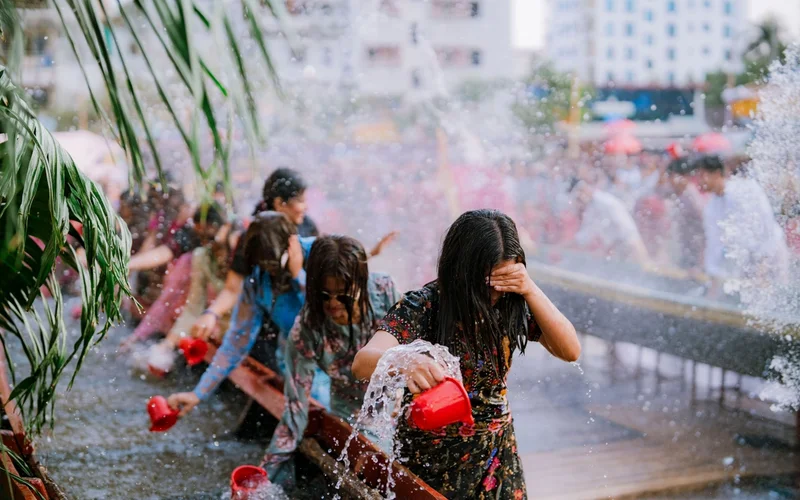 Varias personas en un festival del agua, una de ellas vertiendo agua de un recipiente rojo.
