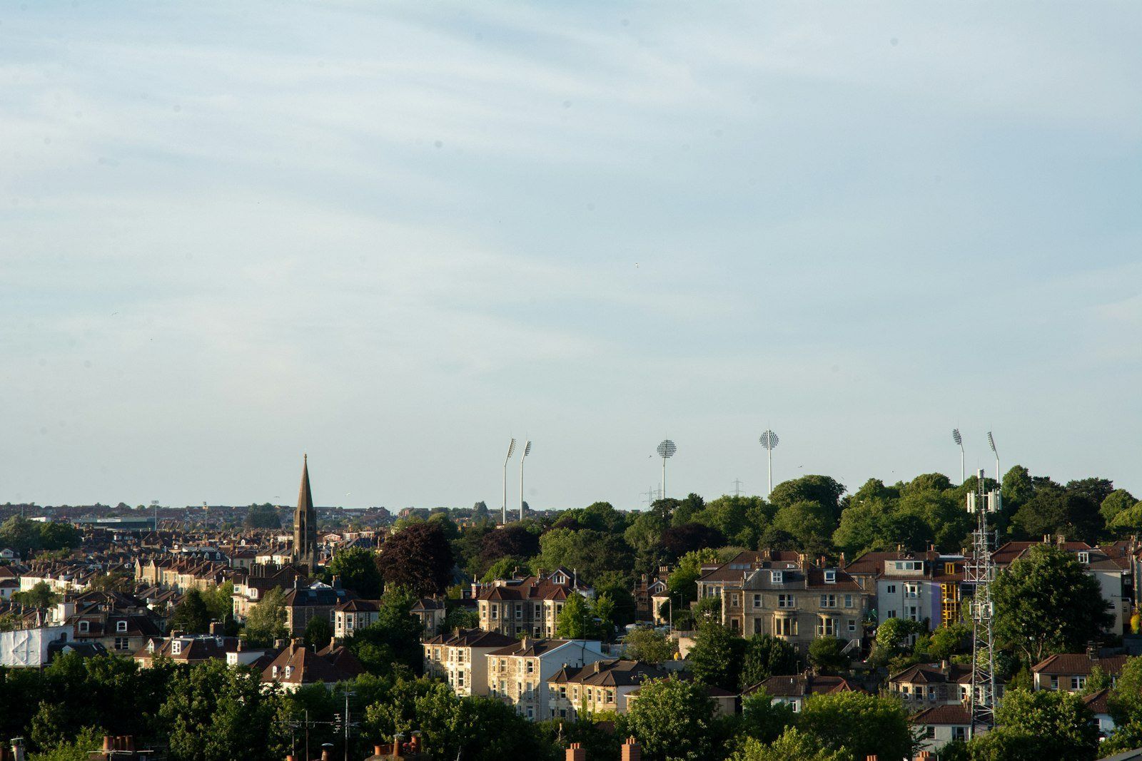 Vista panorámica de Bristol con casas adosadas, árboles frondosos y torre puntiaguda bajo cielo nublado
