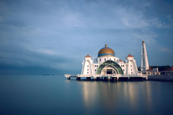 Mezquita flotante de Malaca con cúpula azul y minarete blanco reflejada en el agua al atardecer