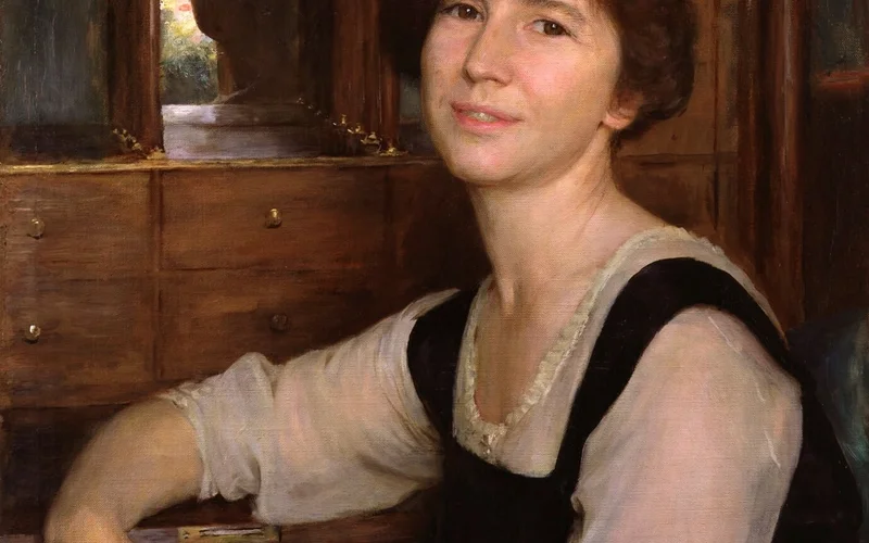 Retrato de Freya Stark sentada ante un escritorio de madera con espejo, cabello corto castaño, blusa blanca y vestido negro