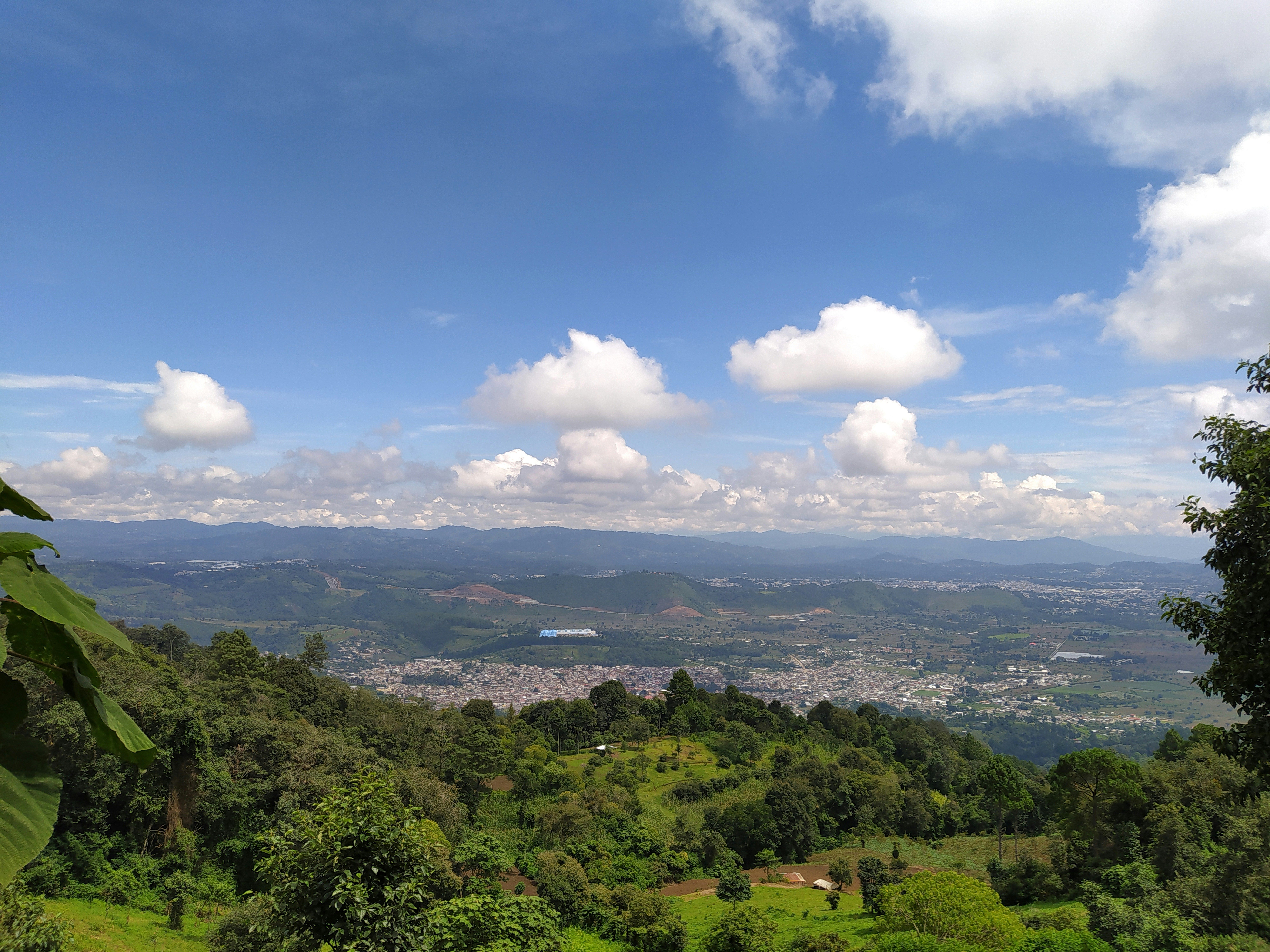 Vista panorámica de un valle montañoso con un pueblo en la distancia bajo un cielo azul con nubes.