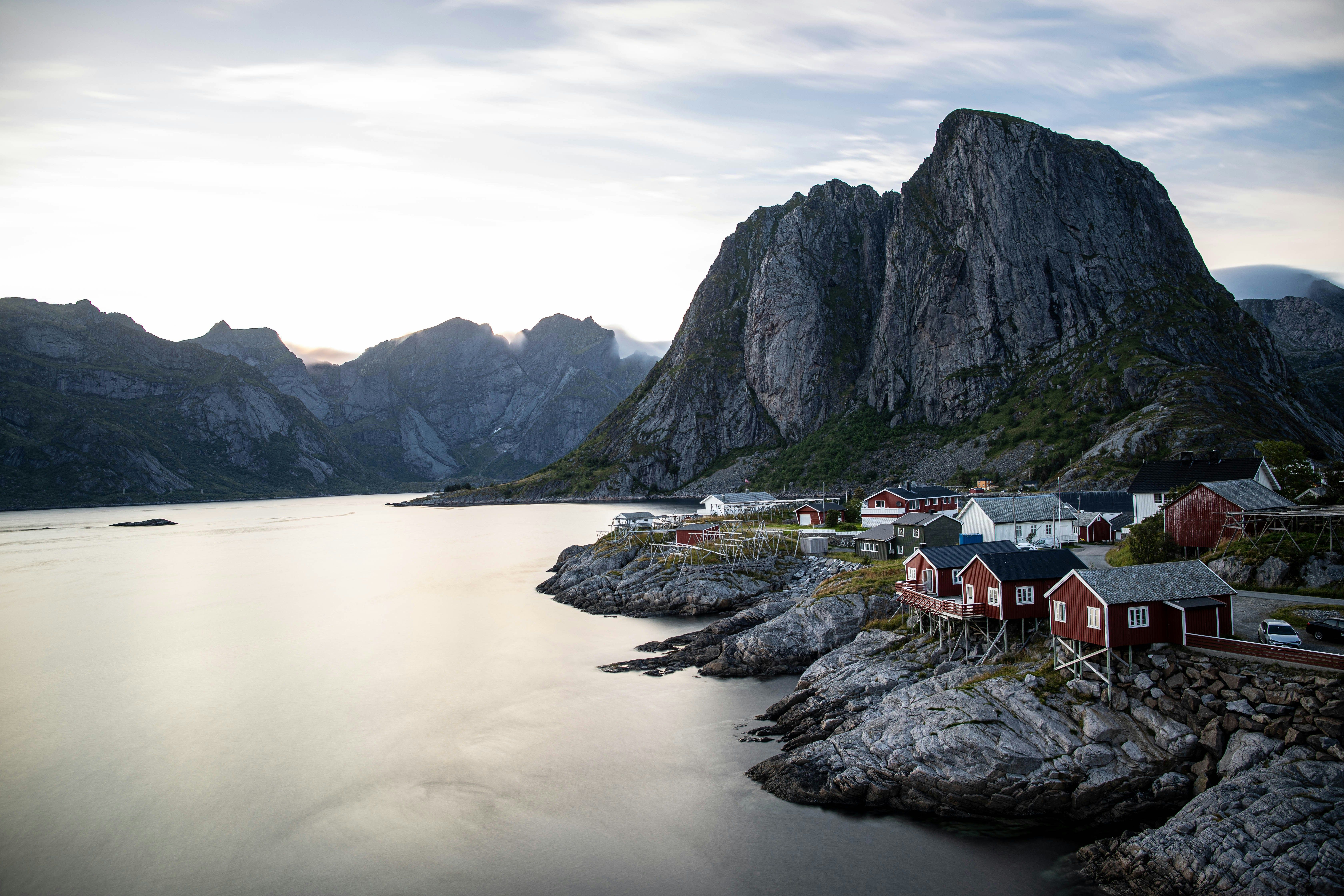 Casas rojas y blancas sobre rocas junto a un fiordo con montañas al fondo bajo un cielo nublado.