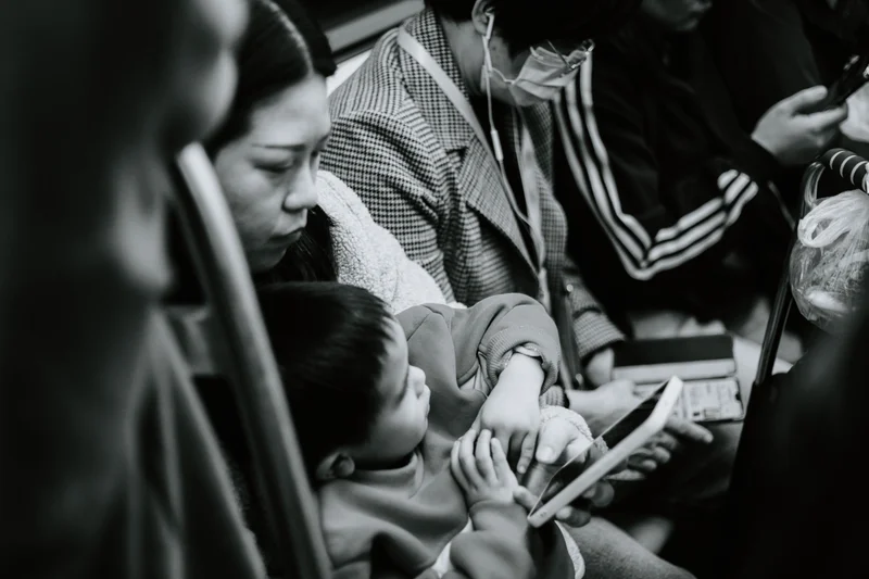 Mujer y niño sentados en un transporte público, el niño mira una pantalla de móvil.