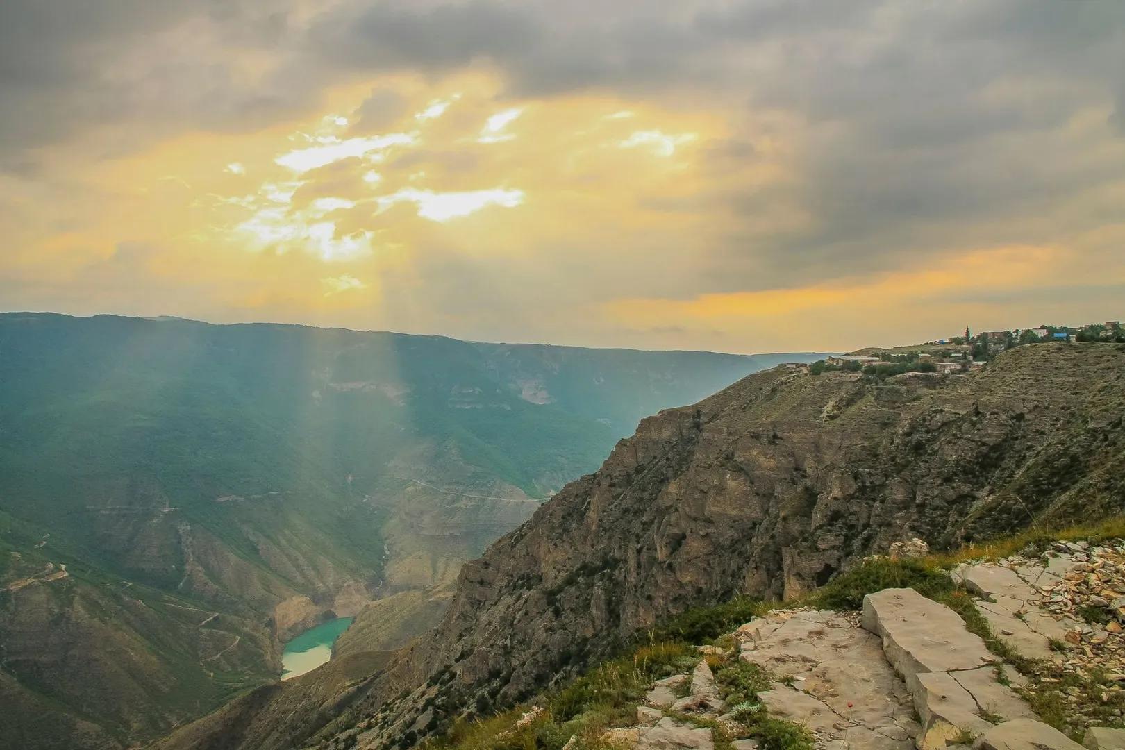 Panorama de cañón profundo en Daguestán con lago turquesa, acantilados rocosos y rayos dorados del sol entre nubes
