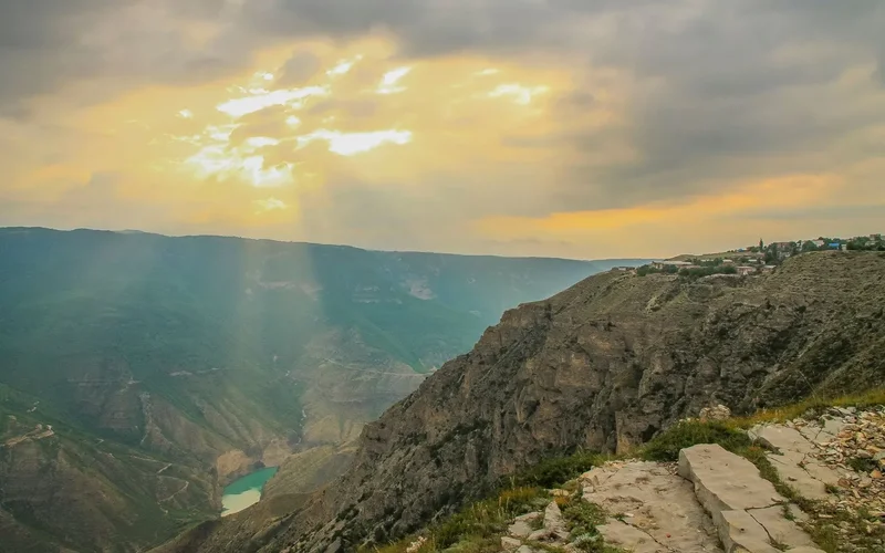 Panorama de cañón profundo en Daguestán con lago turquesa, acantilados rocosos y rayos dorados del sol entre nubes