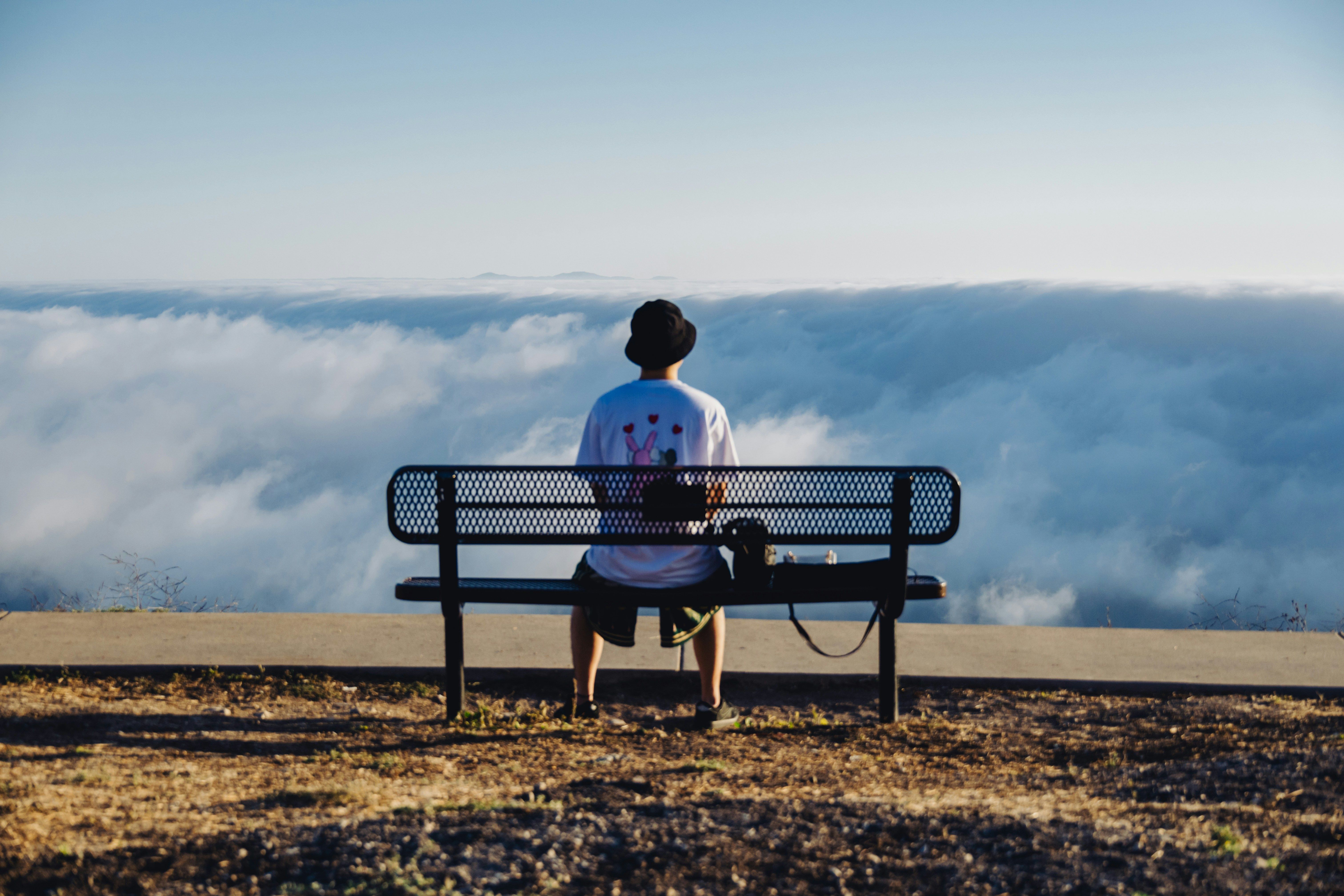 Una persona sentada de espaldas en un banco de metal, mirando un mar de nubes.