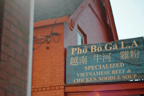 Cartel azul de un restaurante de pho con letras blancas y rojas en un edificio de ladrillo naranja.