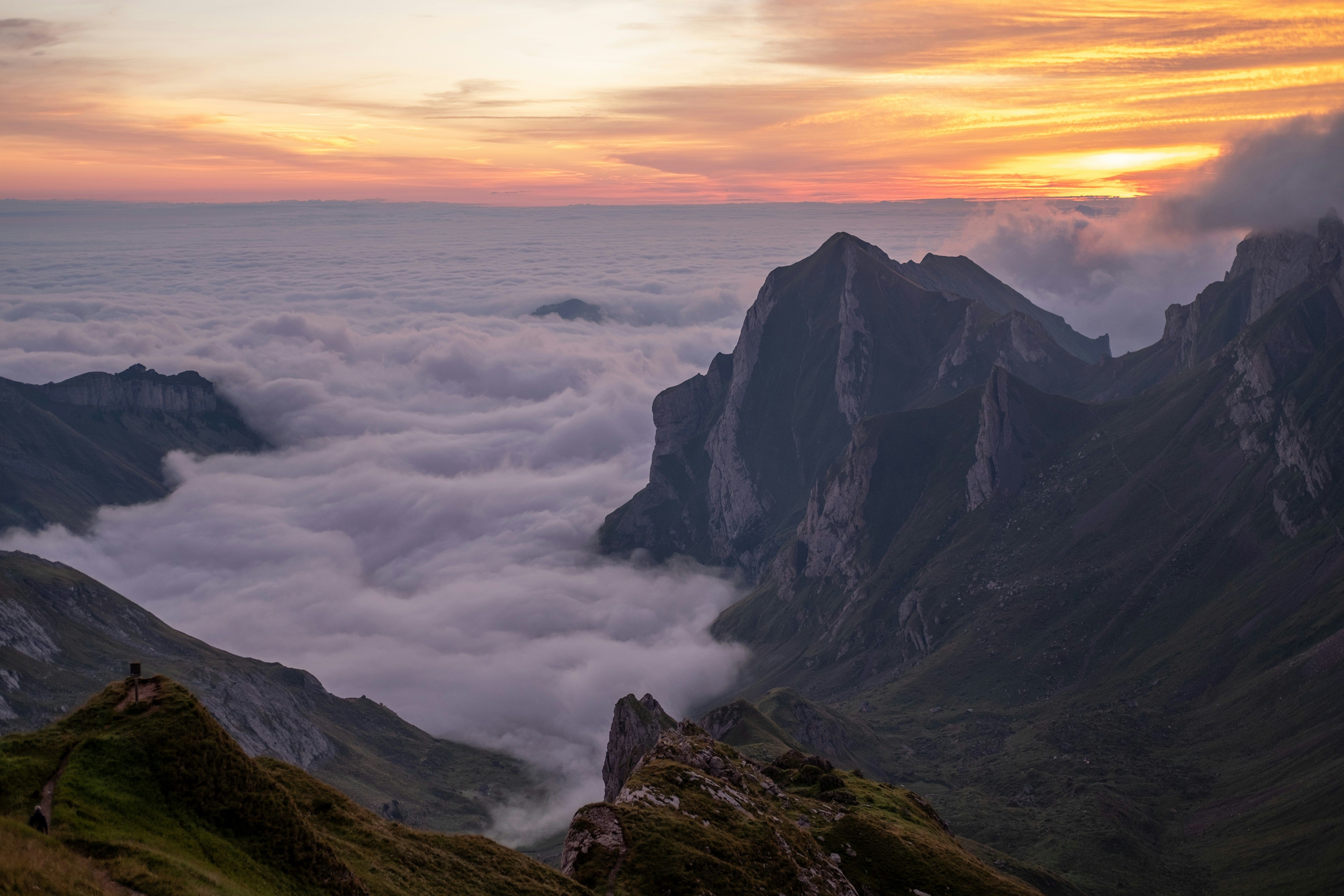 Montañas escarpadas emergiendo de un mar de nubes al atardecer con un cielo anaranjado.