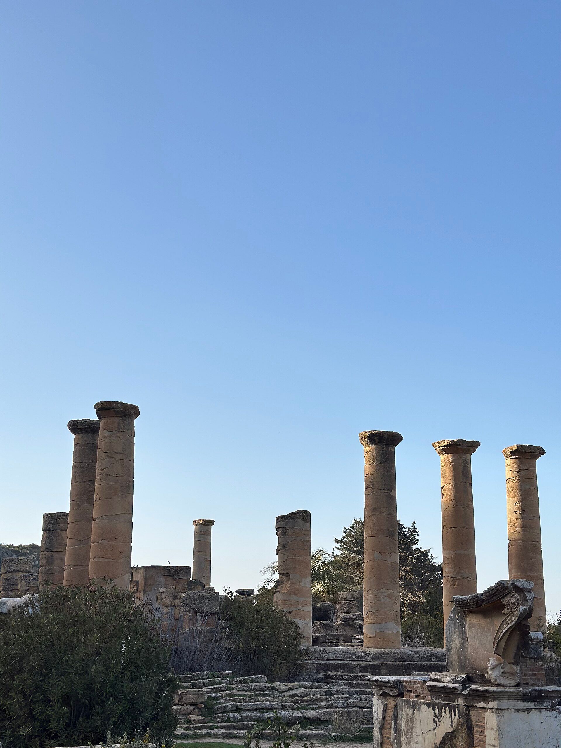 Columnas de piedra antiguas y ruinas de una ciudad bajo un cielo azul claro.