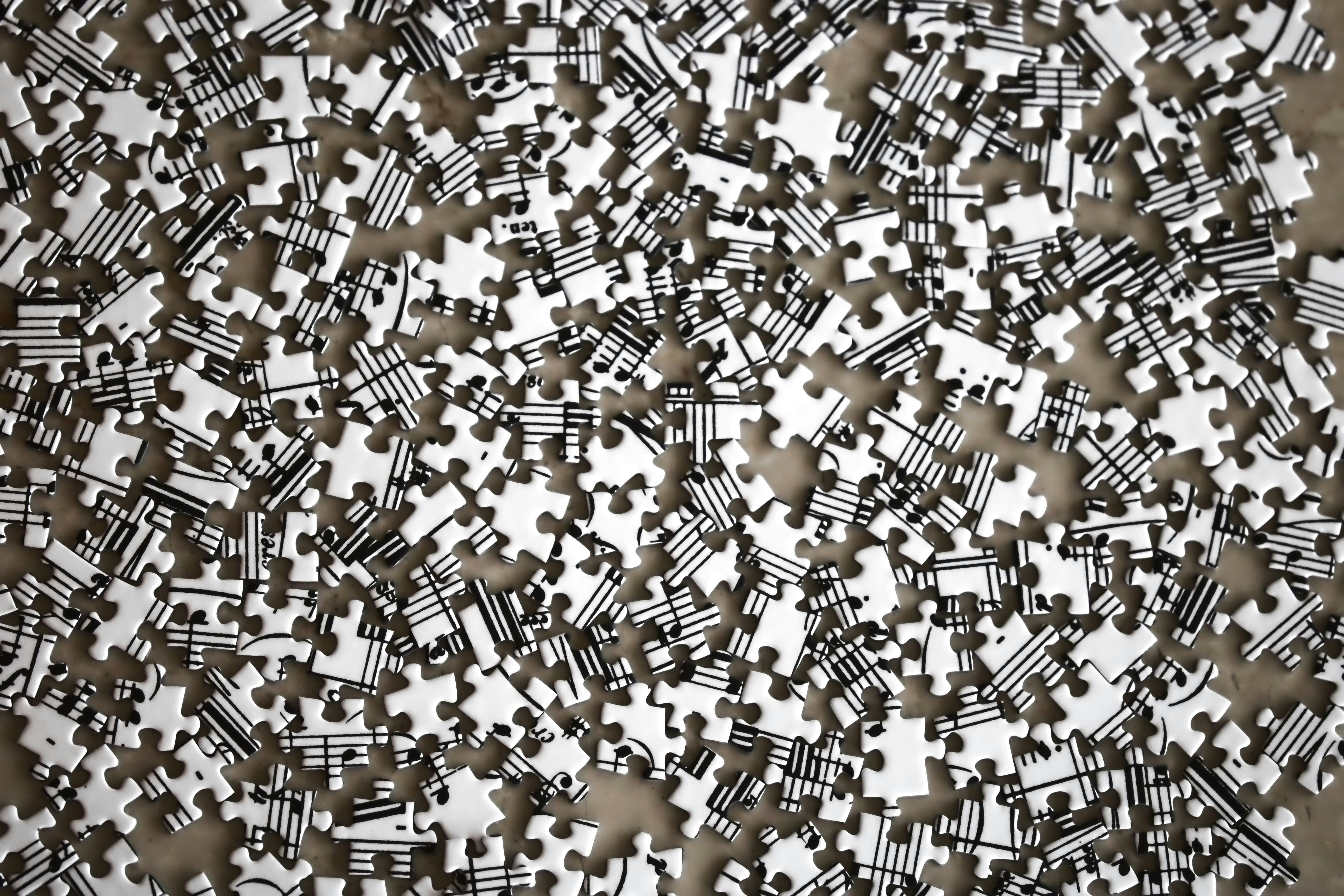 Numerosas piezas de rompecabezas blancas y negras desordenadas, con fragmentos de partituras musicales.