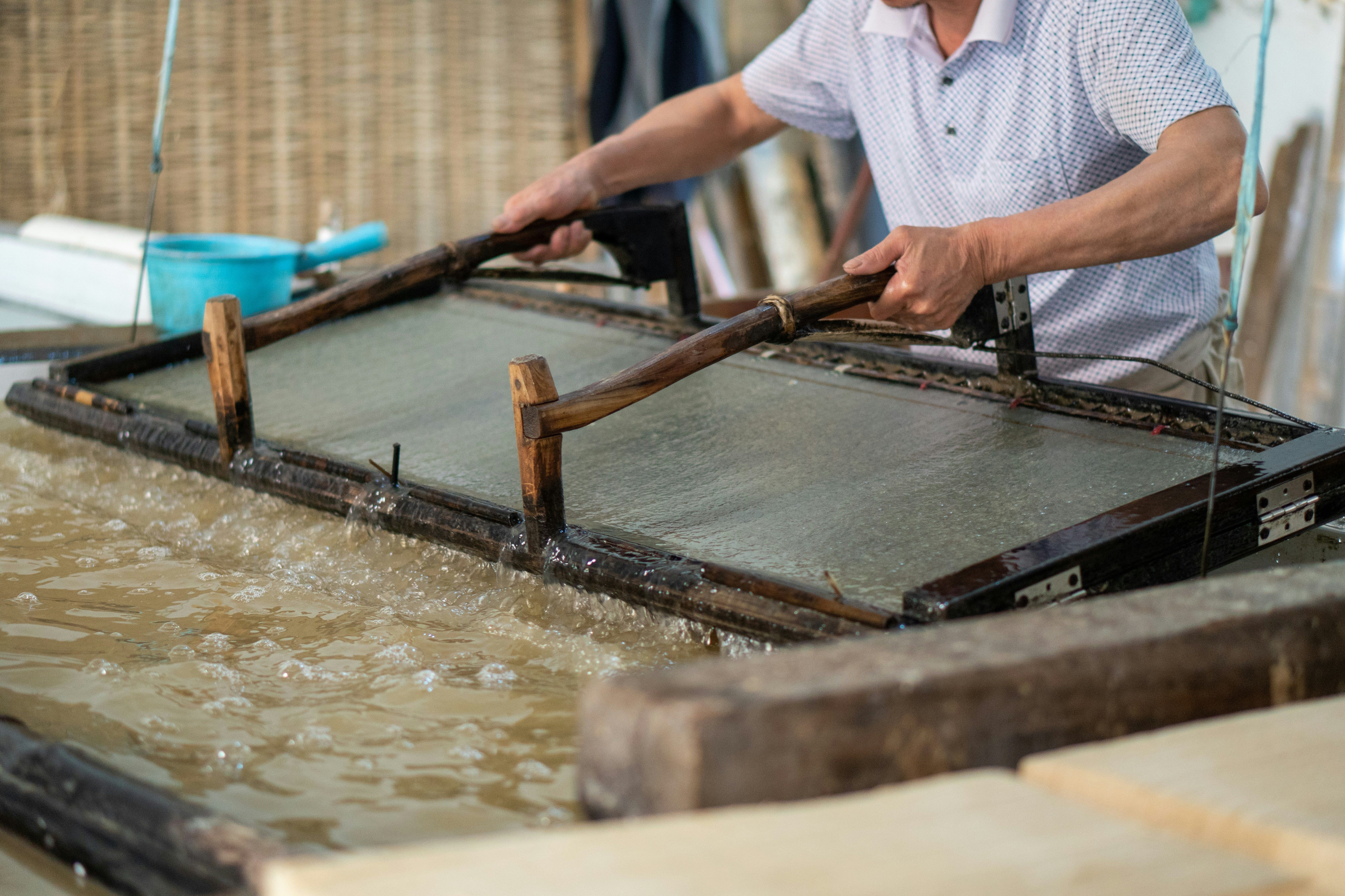 Manos sosteniendo un marco de madera con una malla sumergido en agua espumosa.