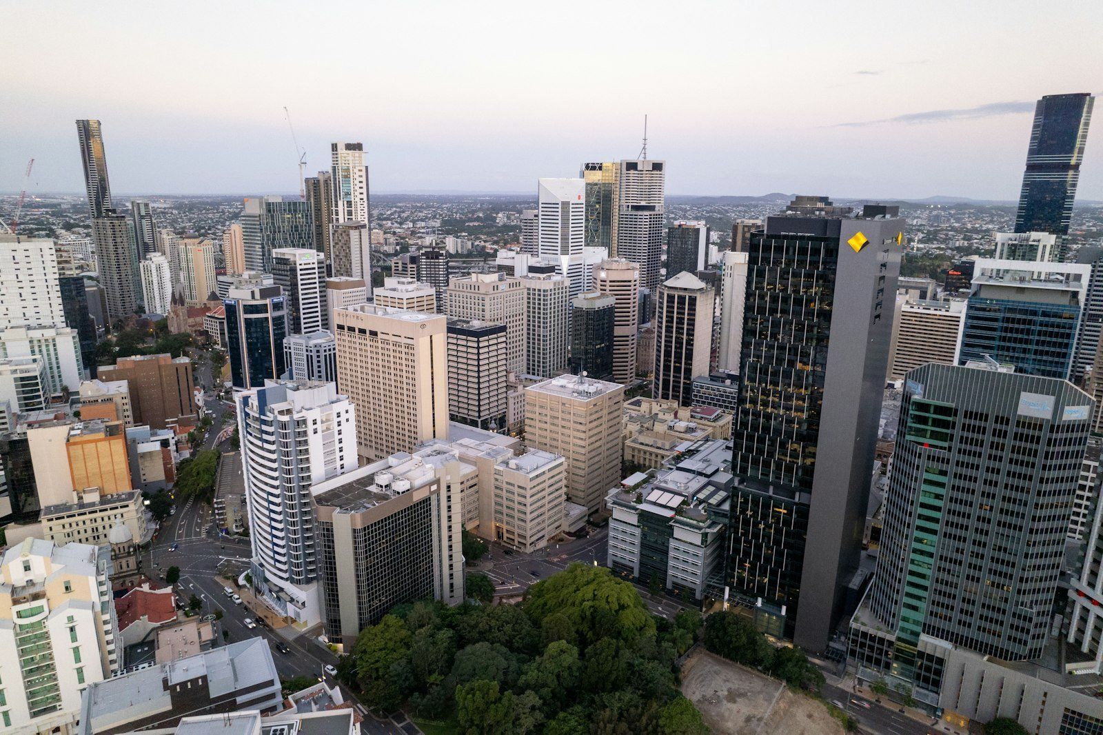 Vista aérea del skyline de Brisbane al atardecer, con rascacielos modernos, vegetación verde y cielo rosado