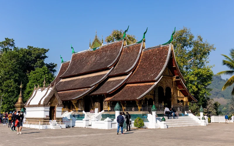 Templo budista de tejados oscuros superpuestos que bajan casi hasta el suelo, con remates verdes y dorados, en una explanada bajo un cielo azul.