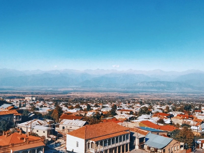 Vista panorámica de Sighnaghi con casas de techos rojos, balcones tradicionales y montañas nevadas del Cáucaso al fondo bajo un cielo azul claro