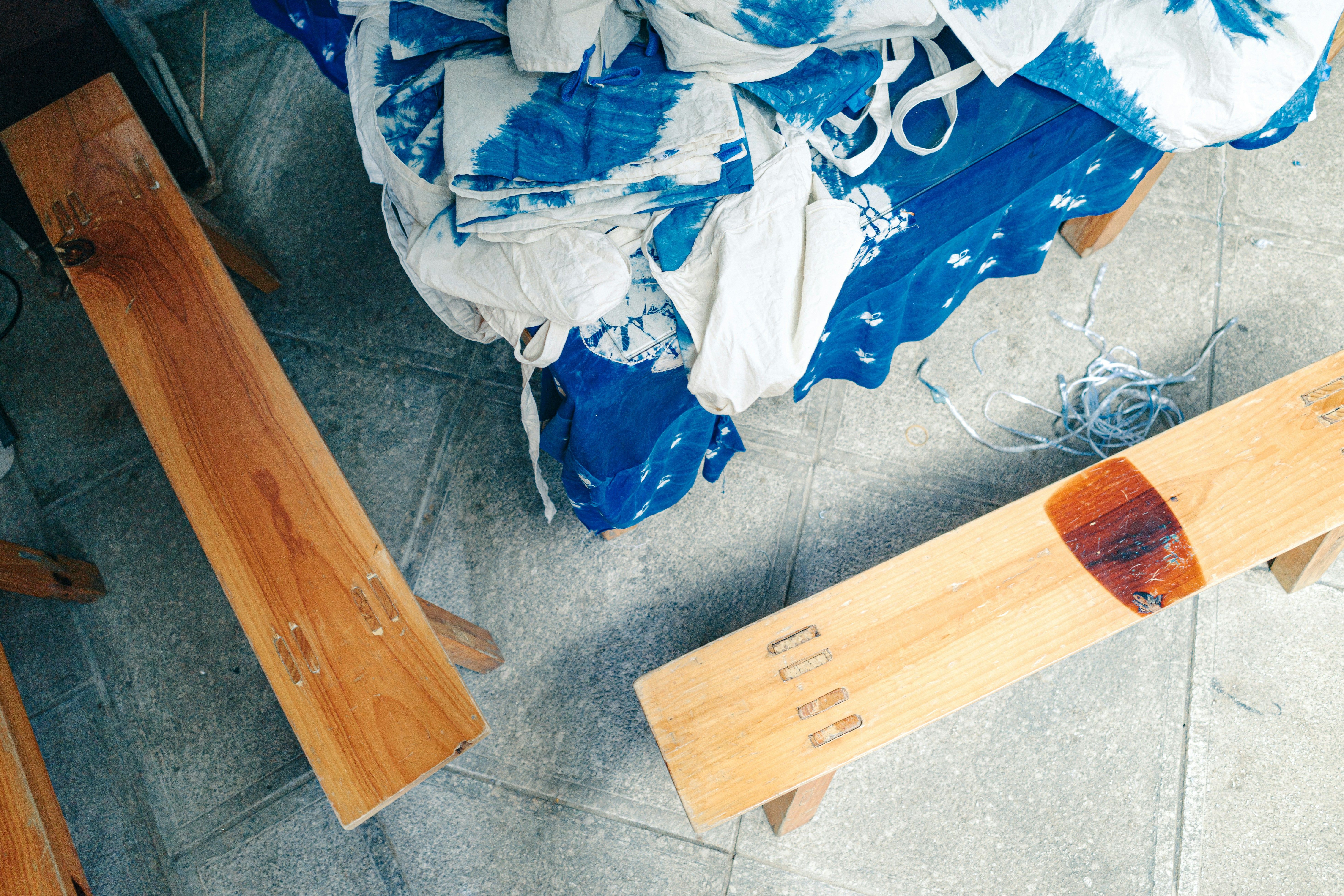 Telas shibori azules y blancas apiladas junto a herramientas de madera sobre un suelo de baldosas.