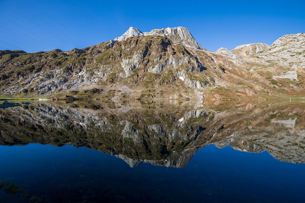 Montañas rocosas y verdes reflejadas perfectamente en la superficie tranquila de un lago azul.