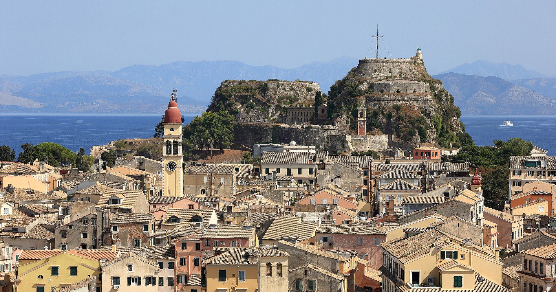 Vista aérea de la ciudad vieja de Corfú con tejados, campanario y una fortaleza junto al mar.