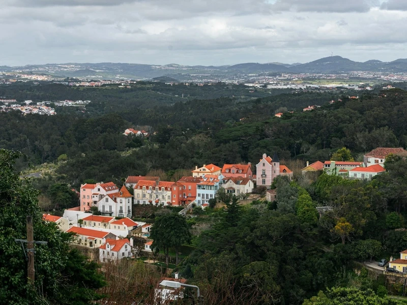 Panorámica de Sintra con edificios coloridos de techos rojos, vegetación verde exuberante y colinas boscosas al fondo bajo un cielo nublado