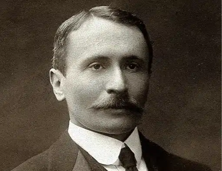 Retrato en blanco y negro de un hombre de mediana edad con bigote, cabello corto peinado y traje formal oscuro con corbata