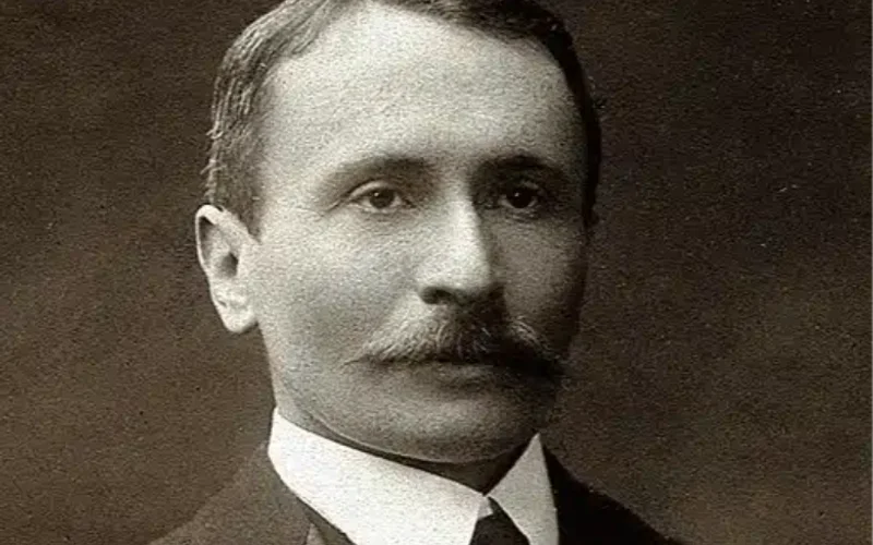 Retrato en blanco y negro de un hombre de mediana edad con bigote, cabello corto peinado y traje formal oscuro con corbata