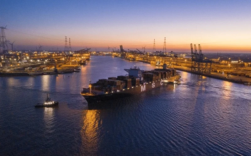 Vista del puerto de Amberes al atardecer con un barco de contenedores MSC navegando entre grúas y muelles iluminados