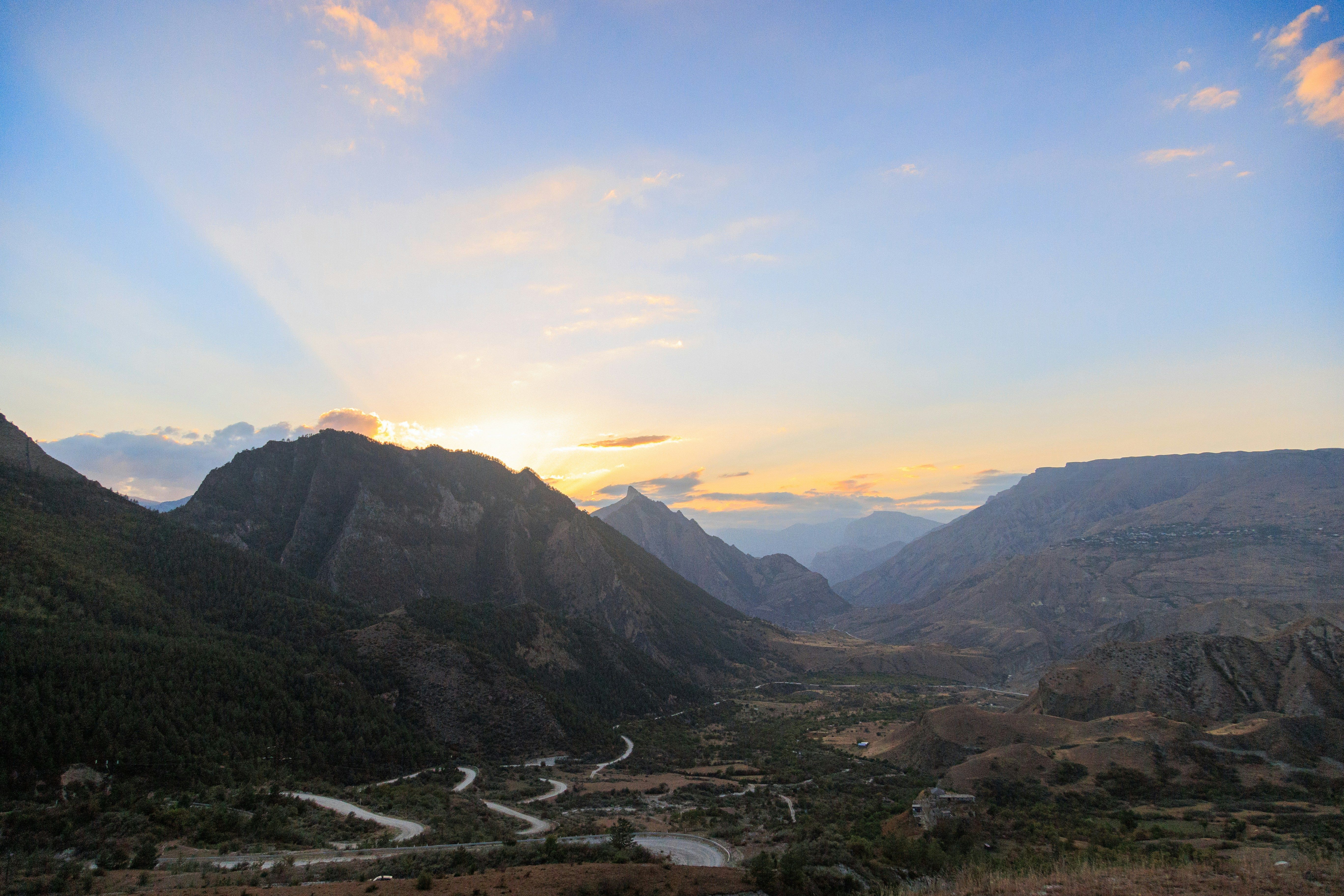 Vista panorámica de un valle montañoso al amanecer, con el sol asomando por detrás de una cumbre.