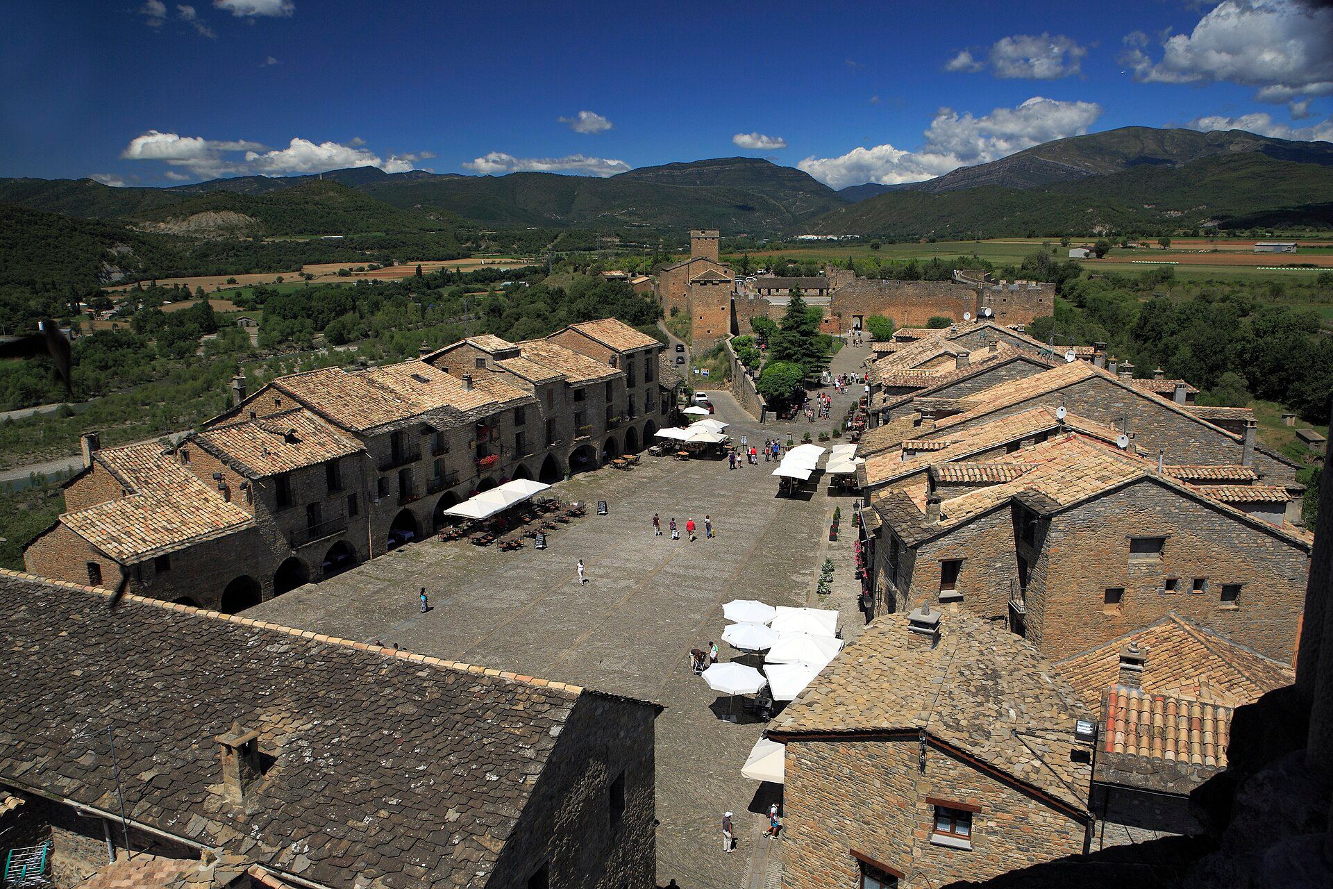 Vista aérea de la Plaza Mayor de Aínsa con edificios de piedra, tejados de teja y montañas al fondo.