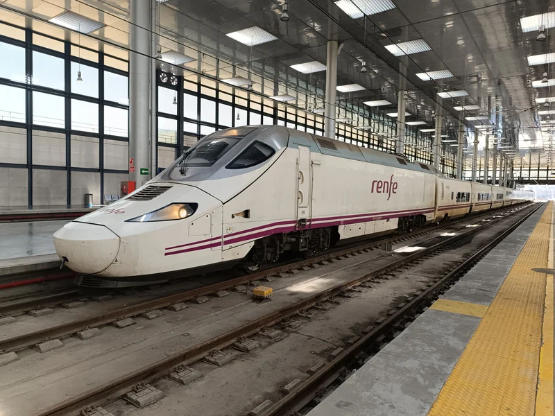 Tren rojo cruzando un viaducto de piedra sobre un valle boscoso con montañas al fondo.
