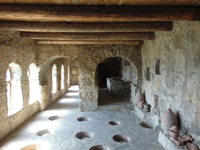 Interior de un edificio antiguo de piedra con arcos, ventanas y agujeros en el suelo, con tinajas.