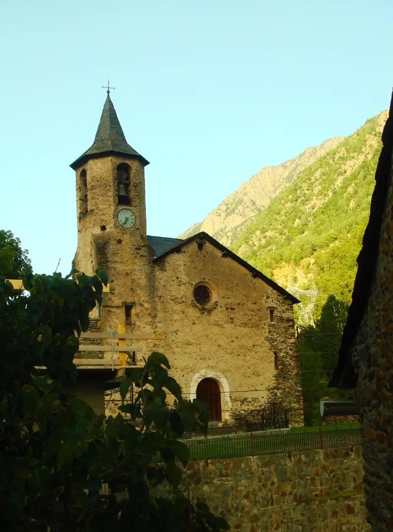Iglesia antigua de piedra con torre campanario y reloj en Tavascan, rodeada de vegetación y montañas pirenaicas al fondo