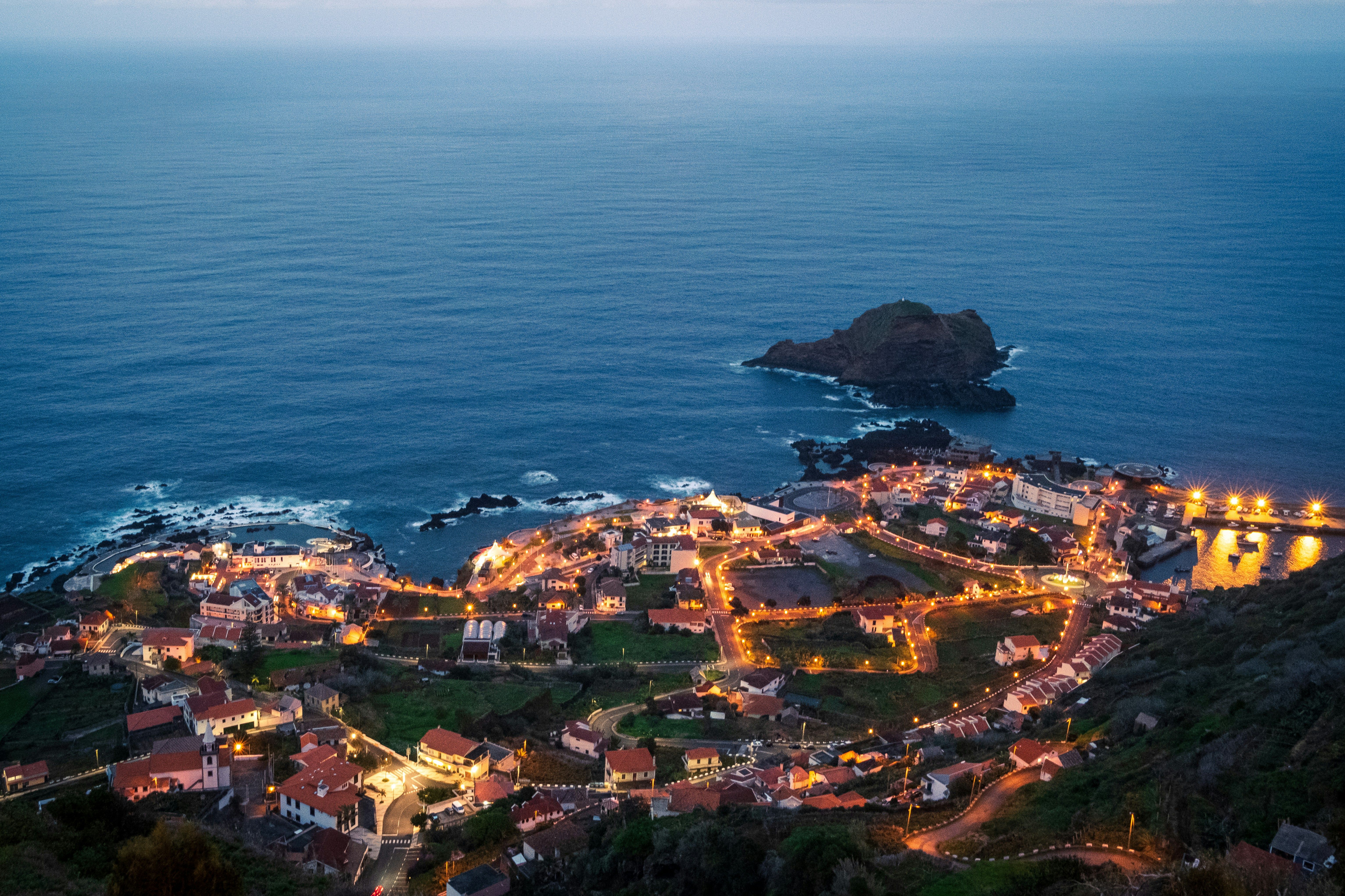 Vista aérea nocturna de un pueblo costero iluminado en Madeira, con el océano Atlántico y un islote.