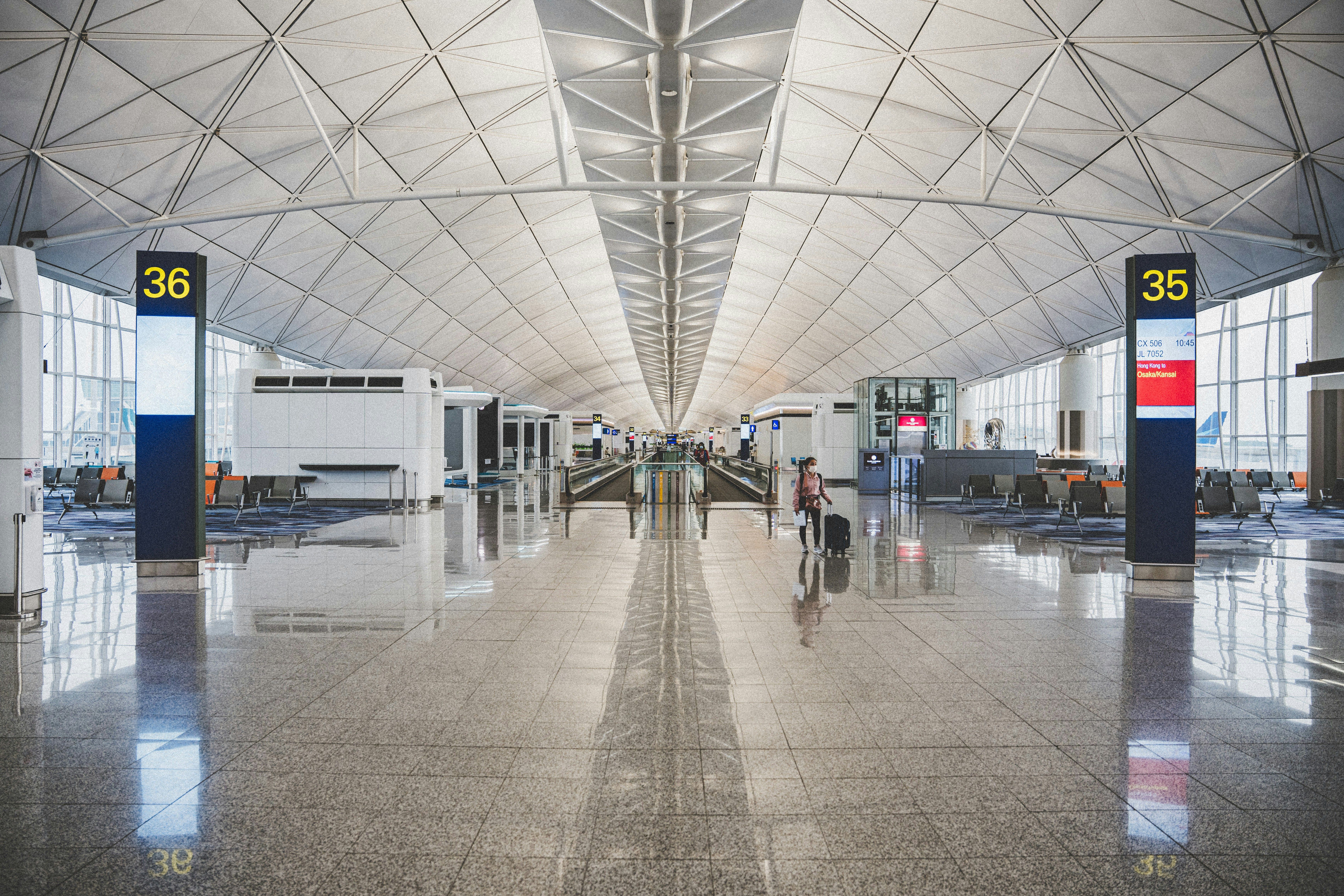 Pasillo de aeropuerto moderno con techo alto y una persona arrastrando una maleta pequeña.