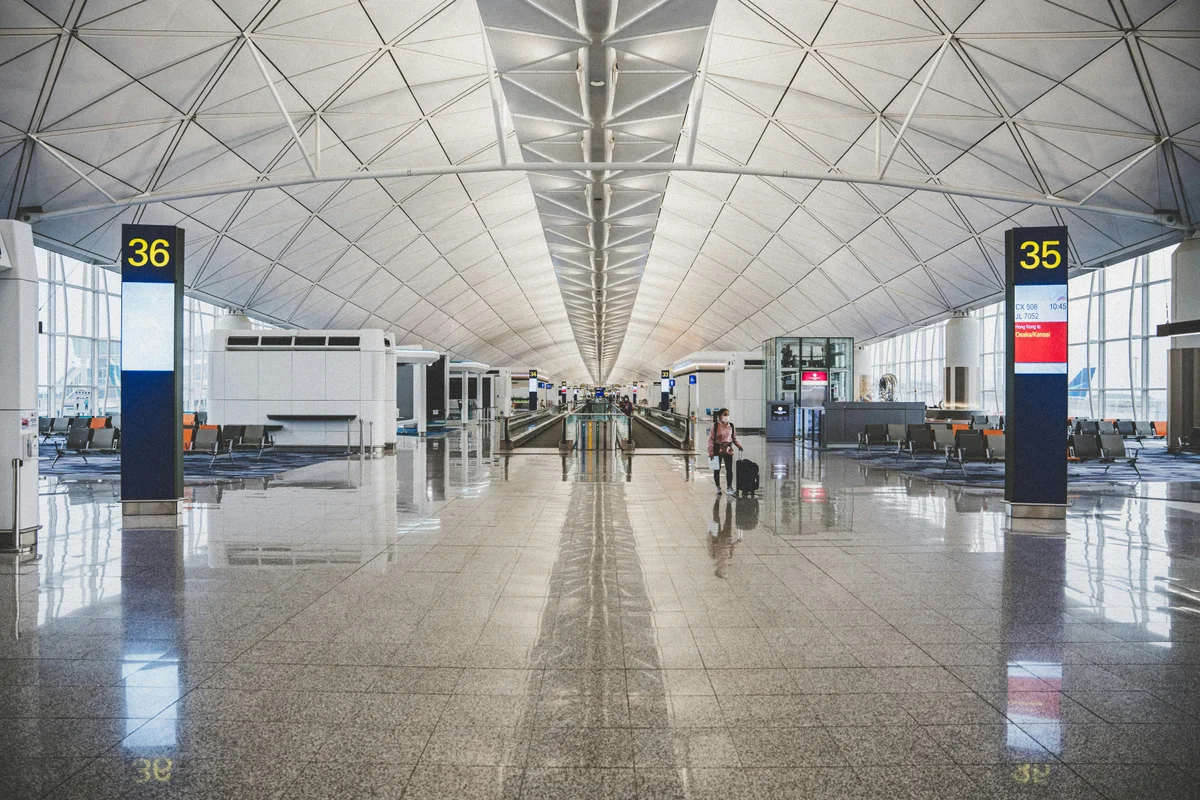 Pasillo de aeropuerto moderno con techo alto y una persona arrastrando una maleta pequeña.