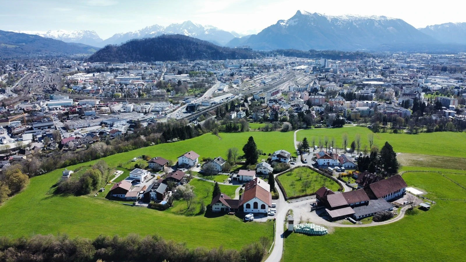 Green field and city meet snow-capped mountains.