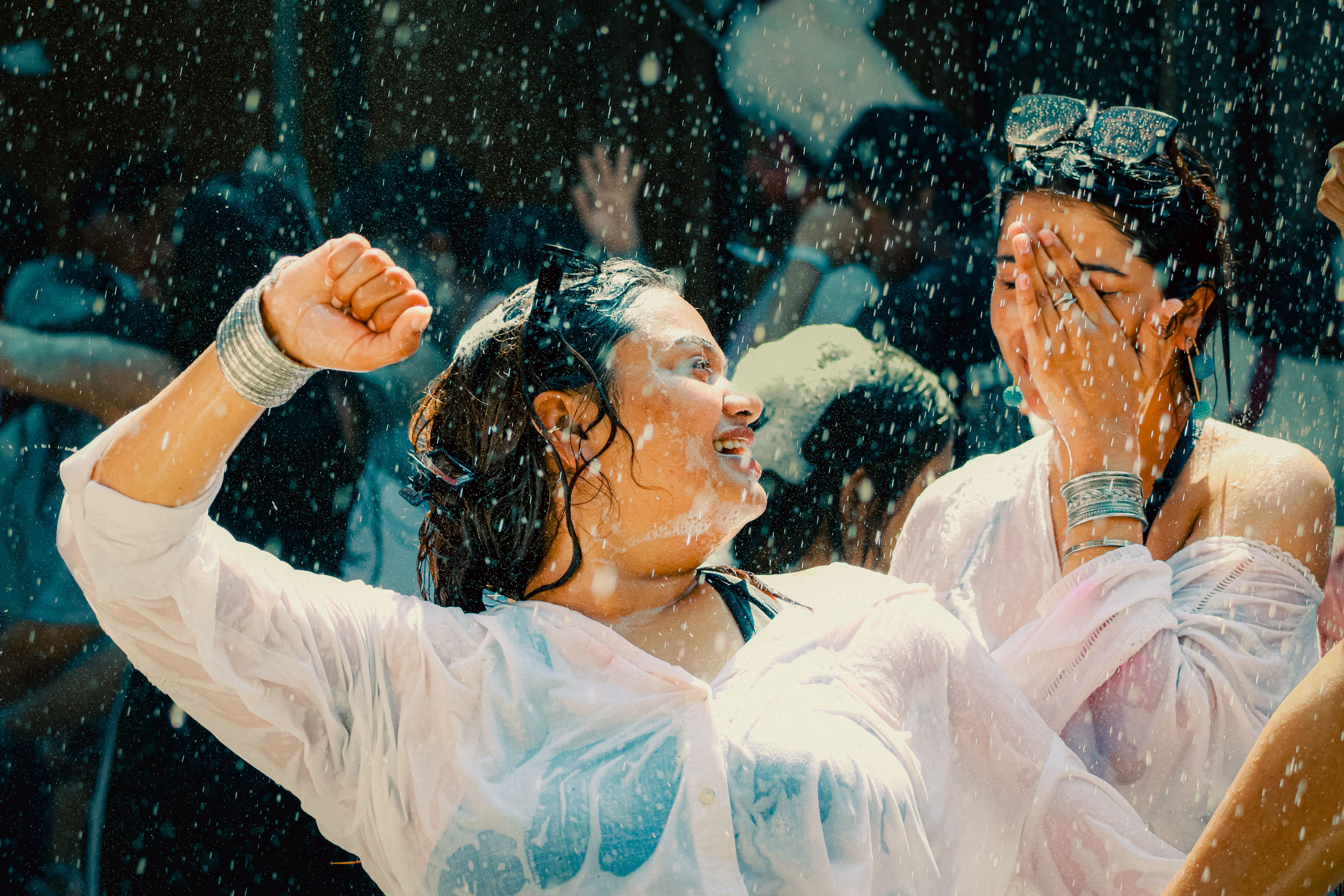 Dos mujeres empapadas de agua y espuma, una sonriendo y la otra cubriéndose la cara.