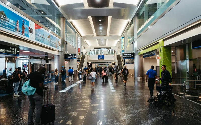 Pasajeros caminando con equipaje de mano en un pasillo amplio y moderno de un aeropuerto.