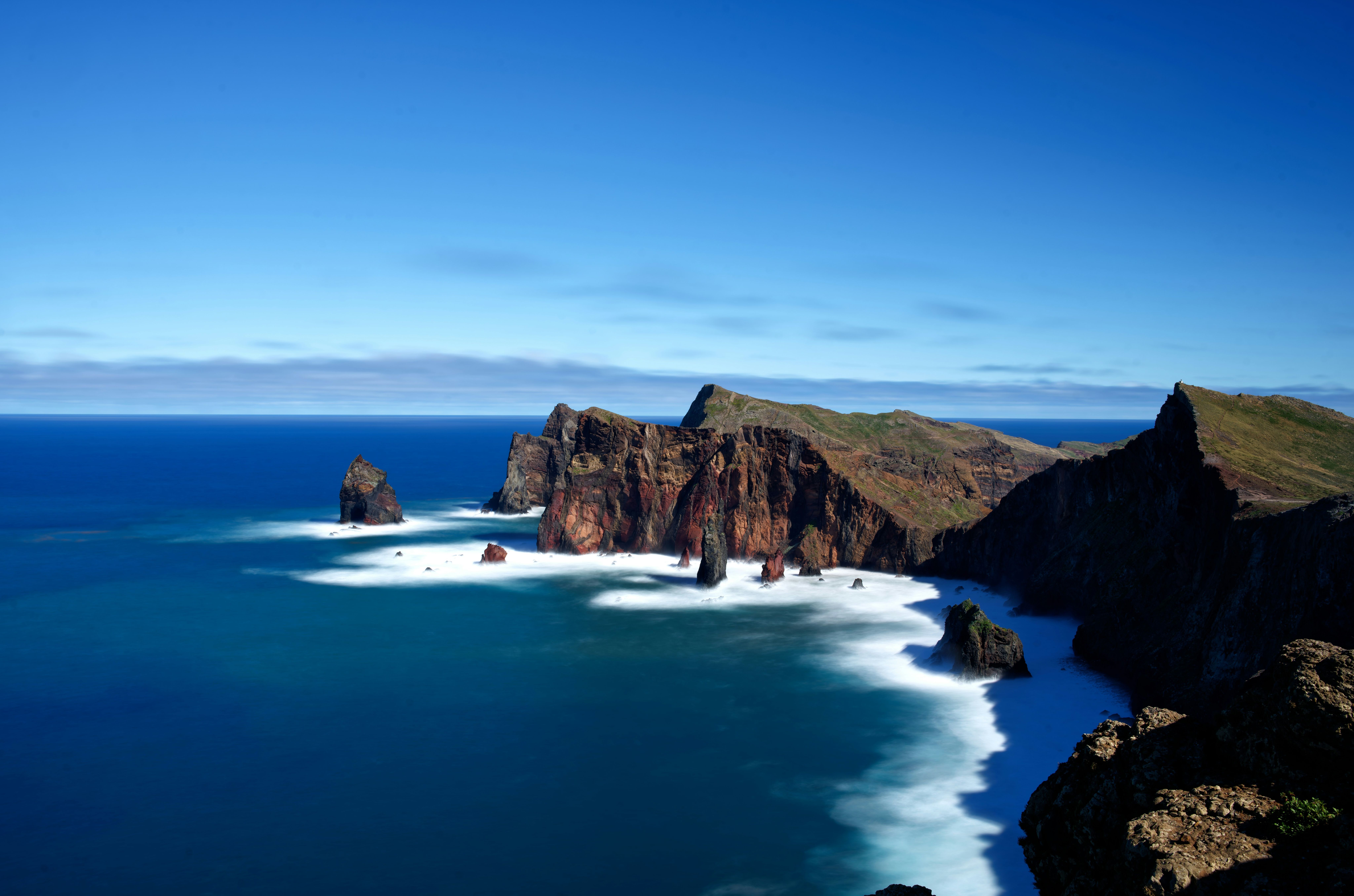 Vista aérea de acantilados rocosos escarpados que se adentran en un océano azul profundo con olas espumosas.